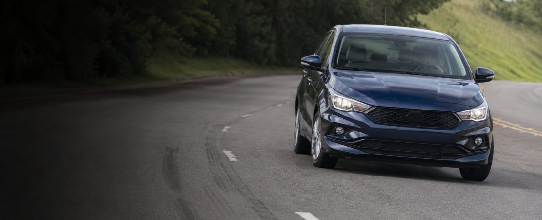 Sedã azul-escuro em curva de estrada, com marcas de frenagem no asfalto