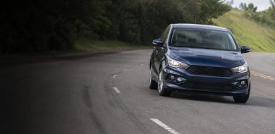 Sedã azul-escuro em curva de estrada, com marcas de frenagem no asfalto