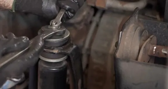 Soltando a porca de fixação do amortecedor de cabine com duas chaves