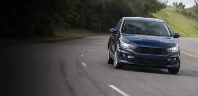 Sedã azul-escuro em curva de estrada, com marcas de frenagem no asfalto